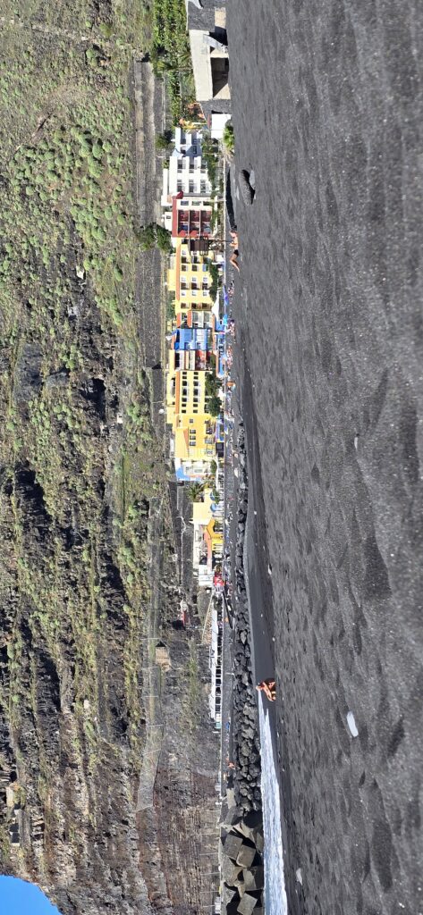 Was man sieht, wenn man flach auf dem Strand liegt. Schwarzer Sand und Häuserskyline, um 90 Grad gedreht